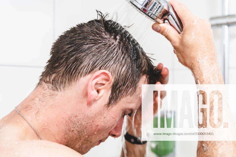 Kiel, Schleswig-Holstein, Germany - 9 July 2023: Young man taking shower with shower head in shower with hot running water