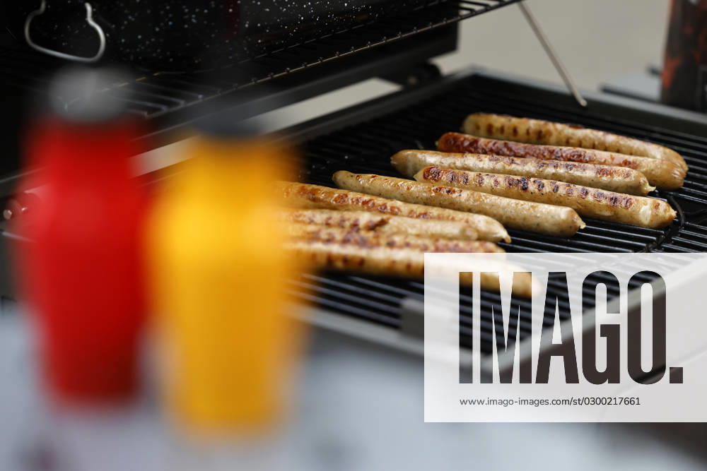 Grilled sausages lie on a coal grill In the foreground ketchup and mustard Theme image, symbol image Cologne, 25 07 2023 NRW Germany