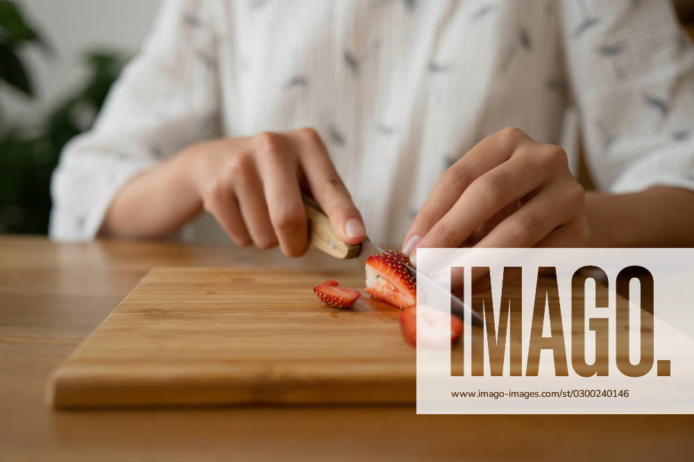 IMAGO Creative, Jahreszeit Sommer, Food, Marmelade kochen PR_ID15648_4255_Room.jpg, MR_ID15648_14434_MayaSolopova.jpg Crop anonymous female in white cloth sitting and cutting red strawberry on board over wooden table while making strawberry jam indoors, Property released MR LiliyaSolopova_ID15648_475515_011