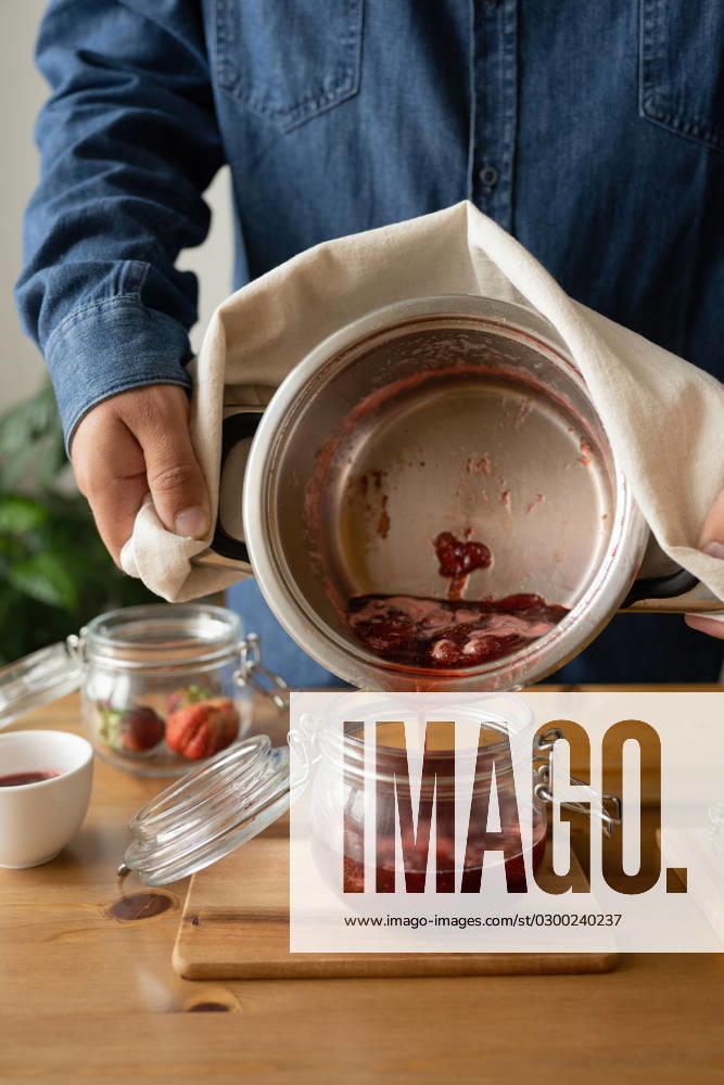 IMAGO Creative, Jahreszeit Sommer, Food, Marmelade kochen PR_ID15648_4255_Room.jpg, MR_ID15648_14436_KonstantinSolopov.jpg Crop anonymous person in casual clothes pouring hot strawberry jam into jar while standing at wooden table with bowl, Property released MR LiliyaSolopova_ID15648_475534_021