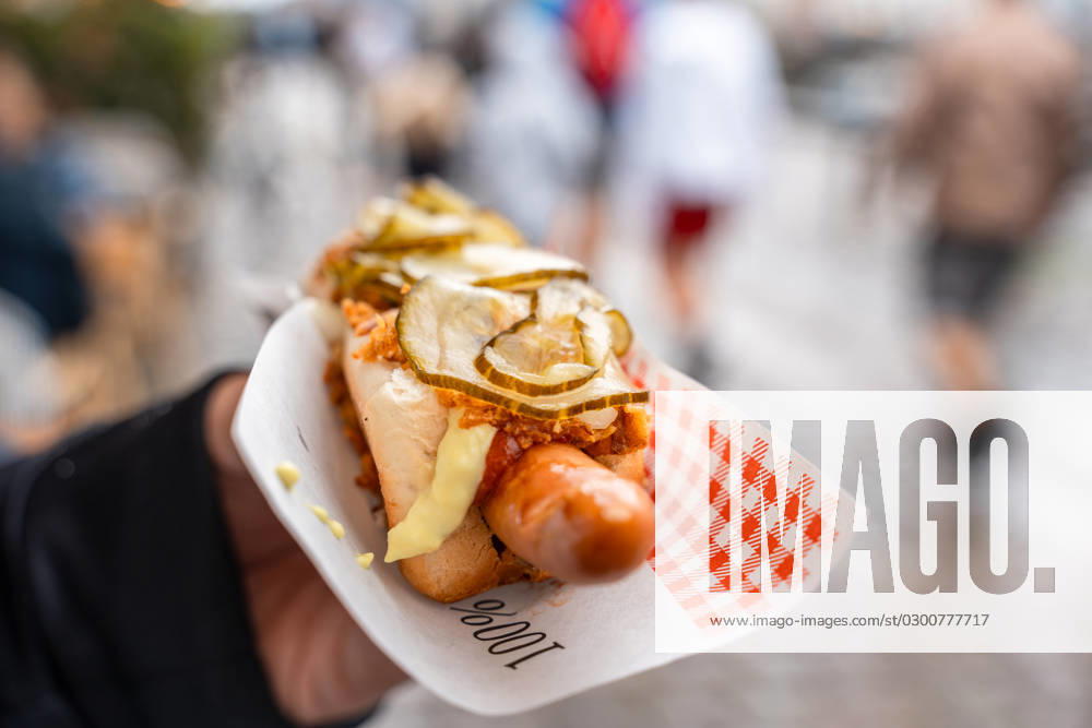 Copenhagen, Denmark - 17 July 2023: Hand holding an original Danish hotdog. Hotdog with sausage, bread, pickles and fried onions in the city