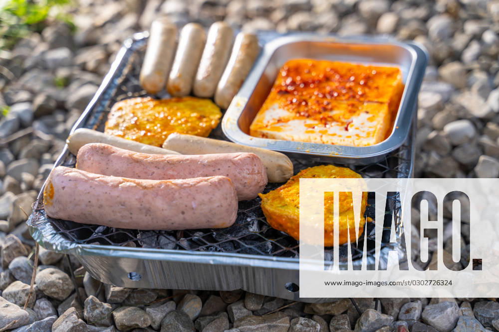 Bavaria, Germany - 2 September 2023: Vegetarian Grilling, Bratwurst Vegan and Vegetarian on a disposable grill on pebbles next to a meadow. Meat and sausage substitutes