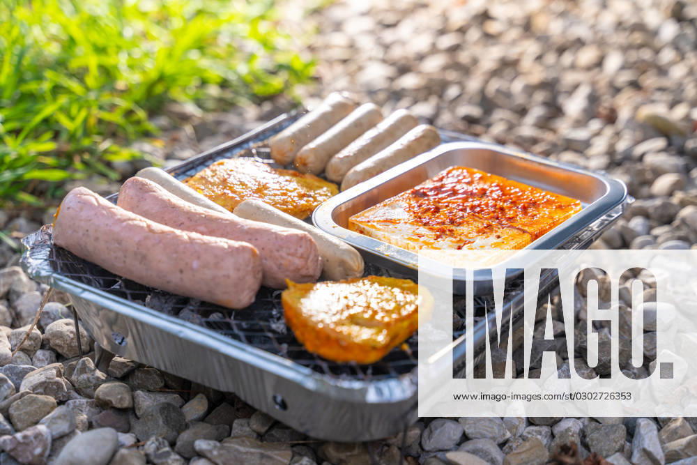 Bavaria, Germany - 2 September 2023: Vegetarian Grilling, Bratwurst Vegan and Vegetarian on a disposable grill on pebbles next to a meadow. Meat and sausage substitutes