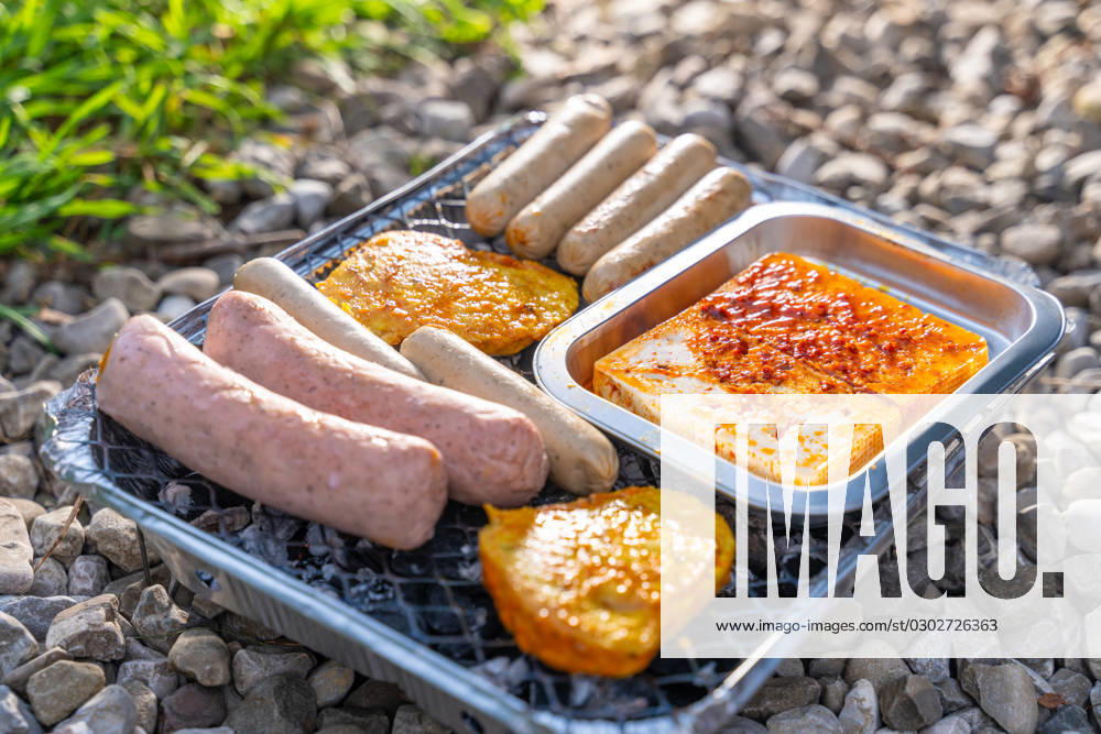 Bavaria, Germany - 2 September 2023: Vegetarian Grilling, Bratwurst Vegan and Vegetarian on a disposable grill on pebbles next to a meadow. Meat and sausage substitutes