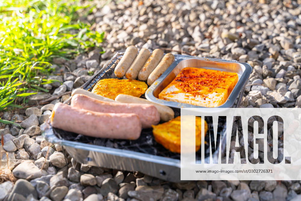 Bavaria, Germany - 2 September 2023: Vegetarian Grilling, Bratwurst Vegan and Vegetarian on a disposable grill on pebbles next to a meadow. Meat and sausage substitutes