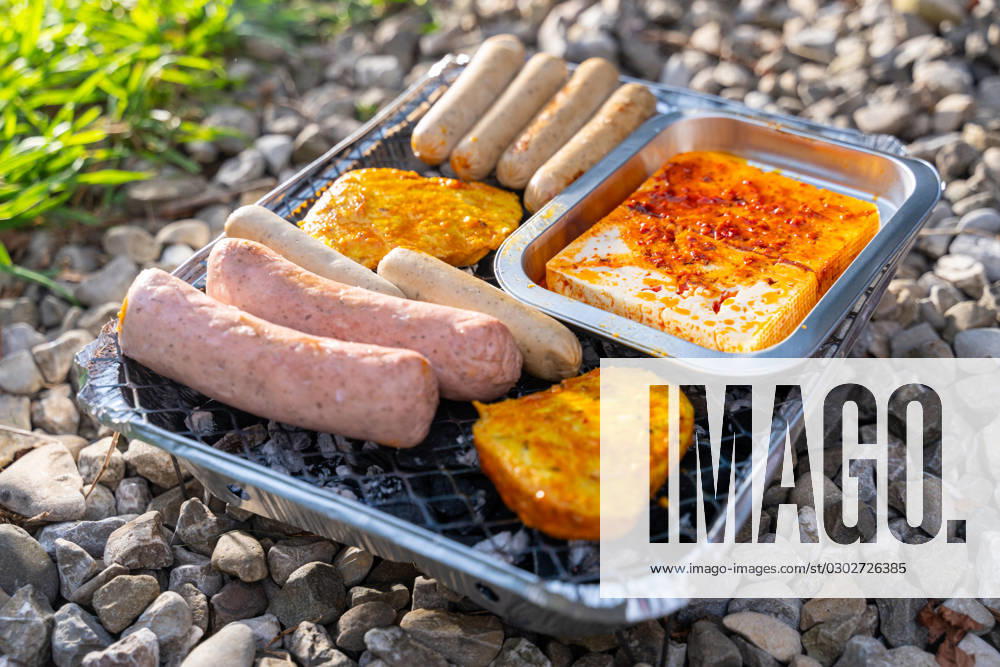 Bavaria, Germany - 2 September 2023: Vegetarian Grilling, Bratwurst Vegan and Vegetarian on a disposable grill on pebbles next to a meadow. Meat and sausage substitutes