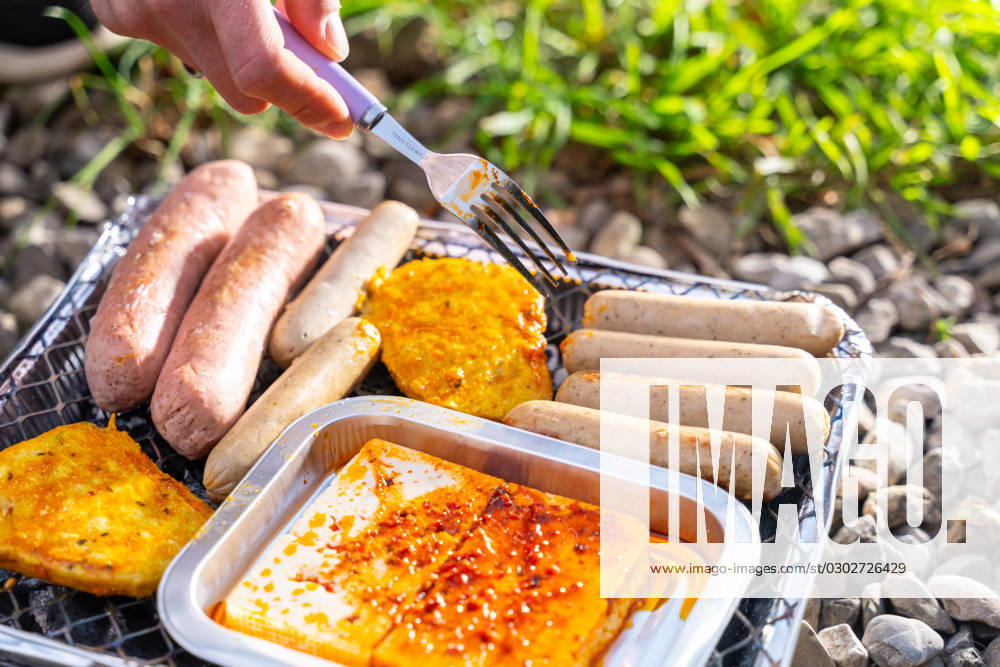 Bavaria, Germany - 2 September 2023: Vegetarian Grilling, Bratwurst Vegan and Vegetarian on a disposable grill. Meat and sausage substitutes. Hand turns grilled food with a fork