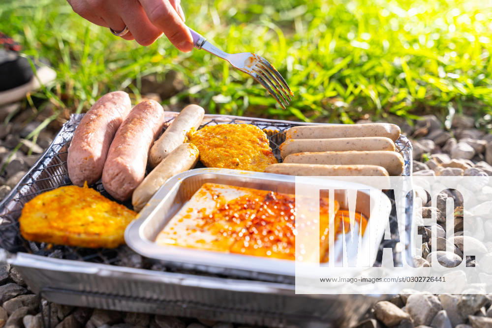 Bavaria, Germany - 2 September 2023: Vegetarian Grilling, Bratwurst Vegan and Vegetarian on a disposable grill. Meat and sausage substitutes. Hand turns grilled food with a fork