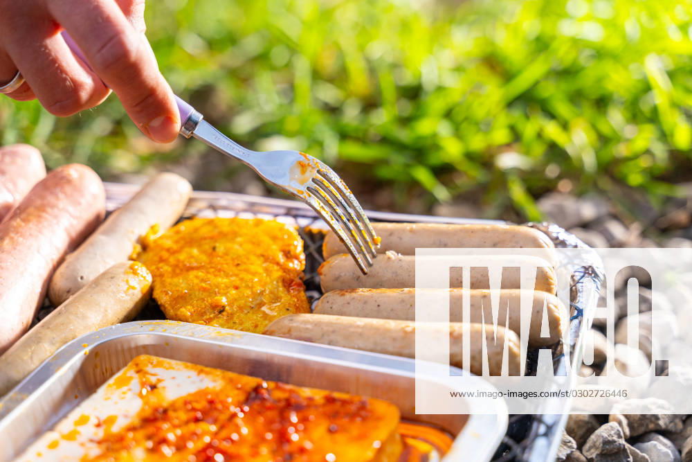 Bavaria, Germany - 2 September 2023: Vegetarian Grilling, Bratwurst Vegan and Vegetarian on a disposable grill. Meat and sausage substitutes. Hand turns grilled food with a fork