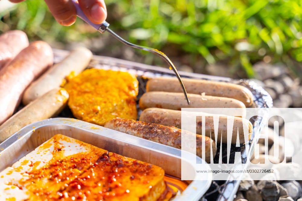 Bavaria, Germany - 2 September 2023: Vegetarian Grilling, Bratwurst Vegan and Vegetarian on a disposable grill. Meat and sausage substitutes. Hand turns grilled food with a fork
