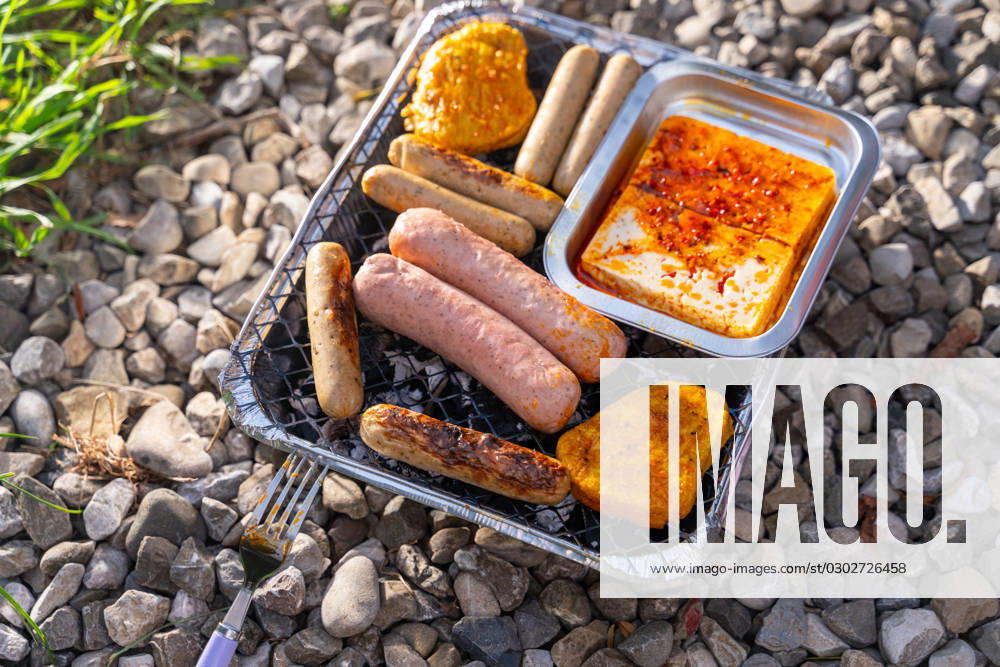 Bavaria, Germany - 2 September 2023: Vegetarian Grilling, Bratwurst Vegan and Vegetarian on a disposable grill on pebbles next to a meadow. Meat and sausage substitutes