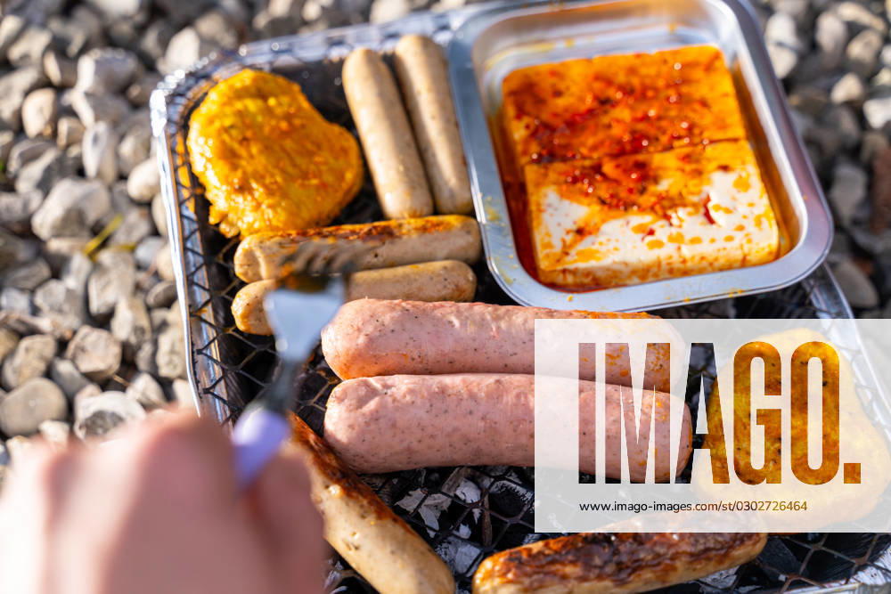 Bavaria, Germany - 2 September 2023: Vegetarian Grilling, Bratwurst Vegan and Vegetarian on a disposable grill. Meat and sausage substitutes. Hand turns grilled food with a fork