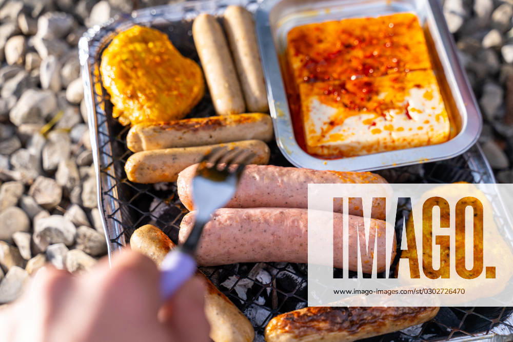 Bavaria, Germany - 2 September 2023: Vegetarian Grilling, Bratwurst Vegan and Vegetarian on a disposable grill. Meat and sausage substitutes. Hand turns grilled food with a fork