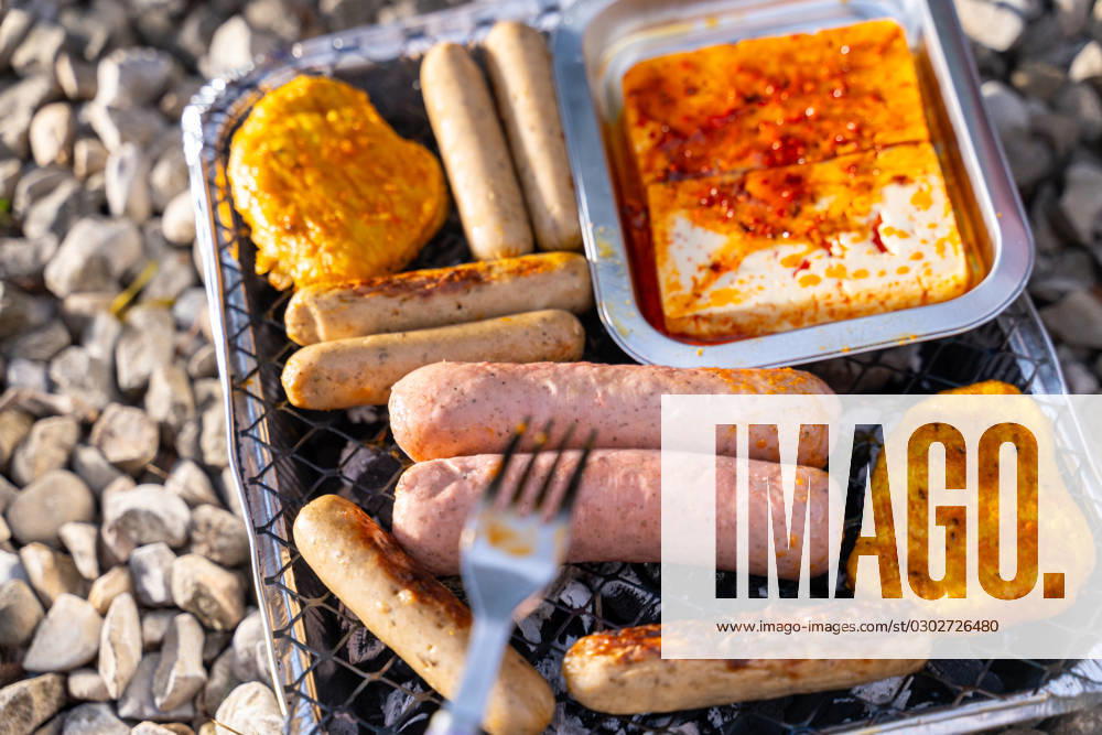 Bavaria, Germany - 2 September 2023: Vegetarian Grilling, Bratwurst Vegan and Vegetarian on a disposable grill. Meat and sausage substitutes. Hand turns grilled food with a fork
