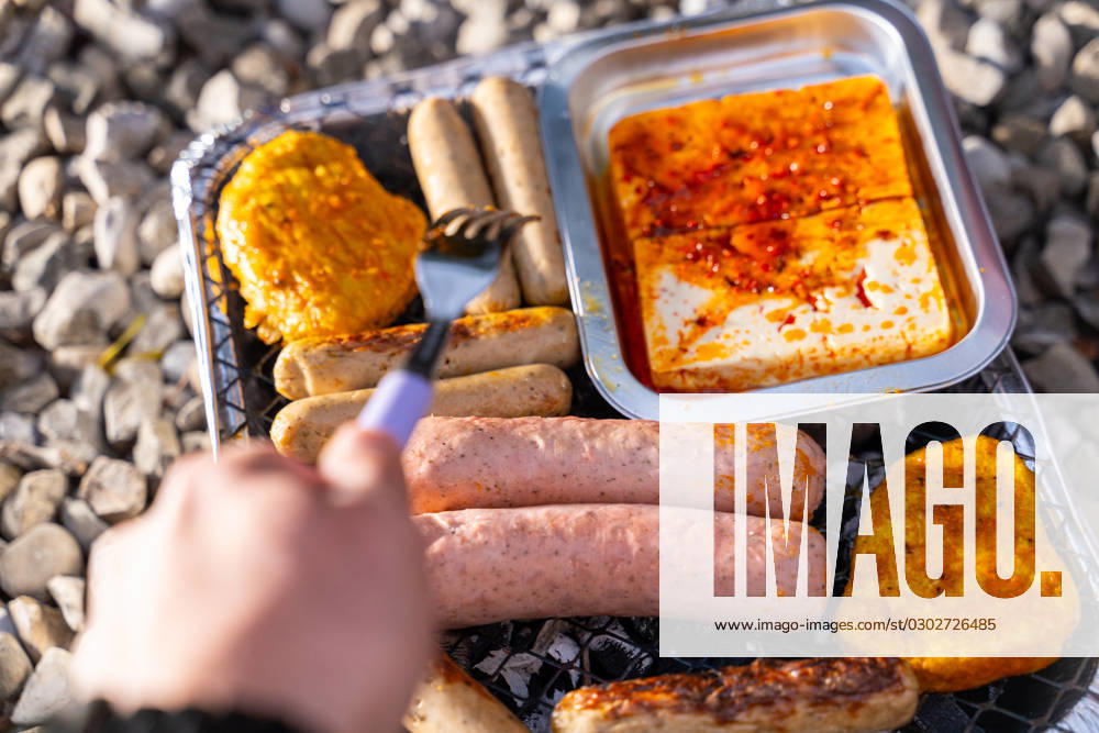 Bavaria, Germany - 2 September 2023: Vegetarian Grilling, Bratwurst Vegan and Vegetarian on a disposable grill. Meat and sausage substitutes. Hand turns grilled food with a fork