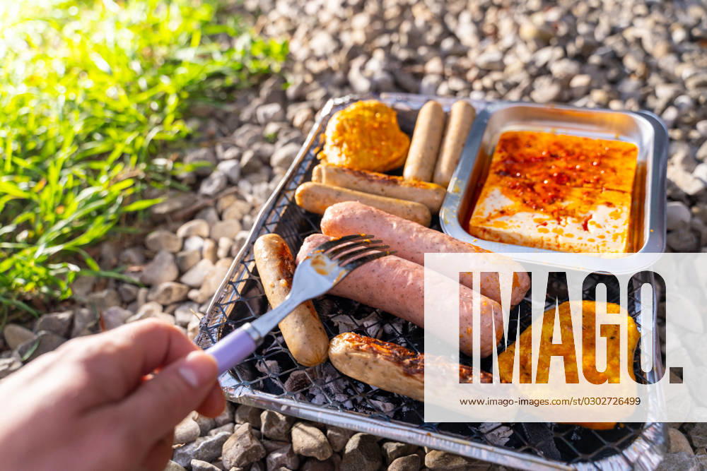 Bavaria, Germany - 2 September 2023: Vegetarian Grilling, Bratwurst Vegan and Vegetarian on a disposable grill. Meat and sausage substitutes. Hand turns grilled food with a fork