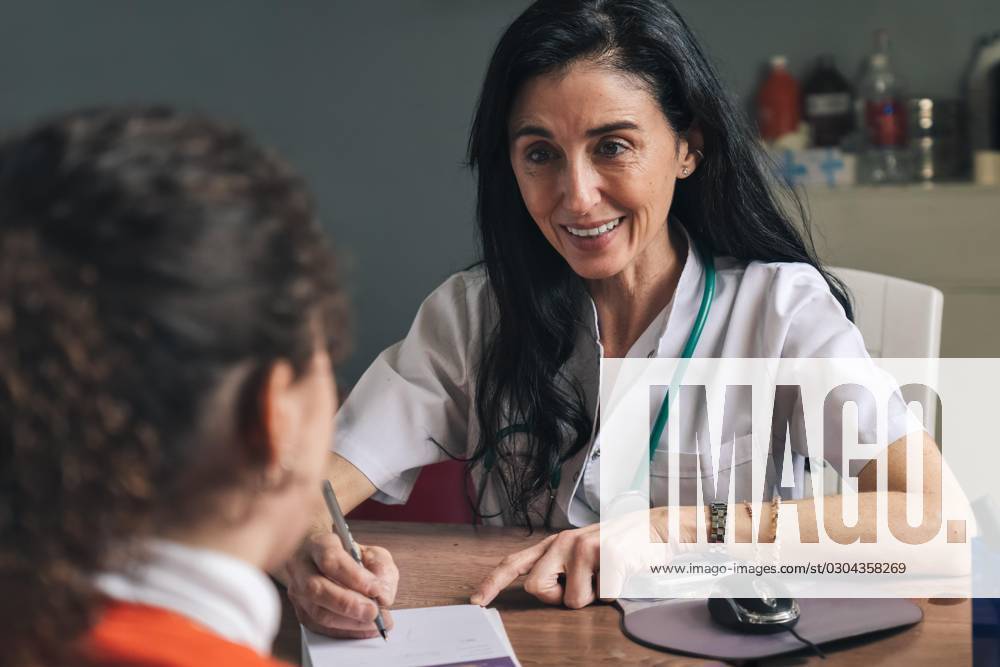 Smiling Doctor with Stethoscope at Interview with a Woman at Hospital in a Medical practice and at write one Recipe