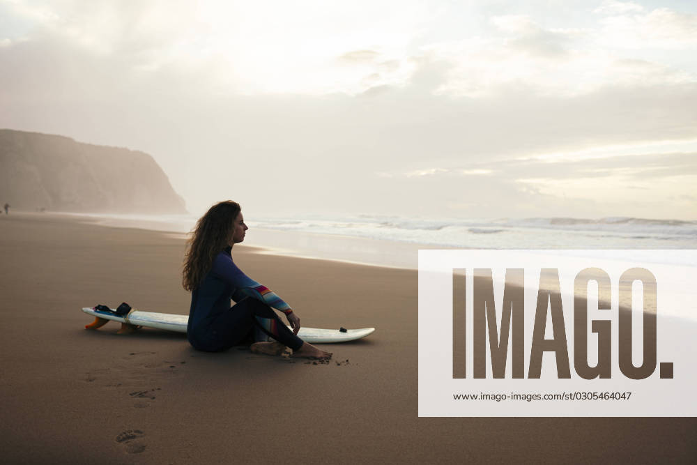 Thoughtful woman with surfboard sitting at beach model released, Symbolfoto, DCRF01769