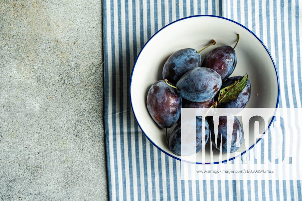 IMAGO Creative, Jahreszeit Sommer, Food, Pflaume Top view of ripe plums served in ceramic bowl on striped napkin against gray surface Model Released AnnaBogush_ID17000_518396_004