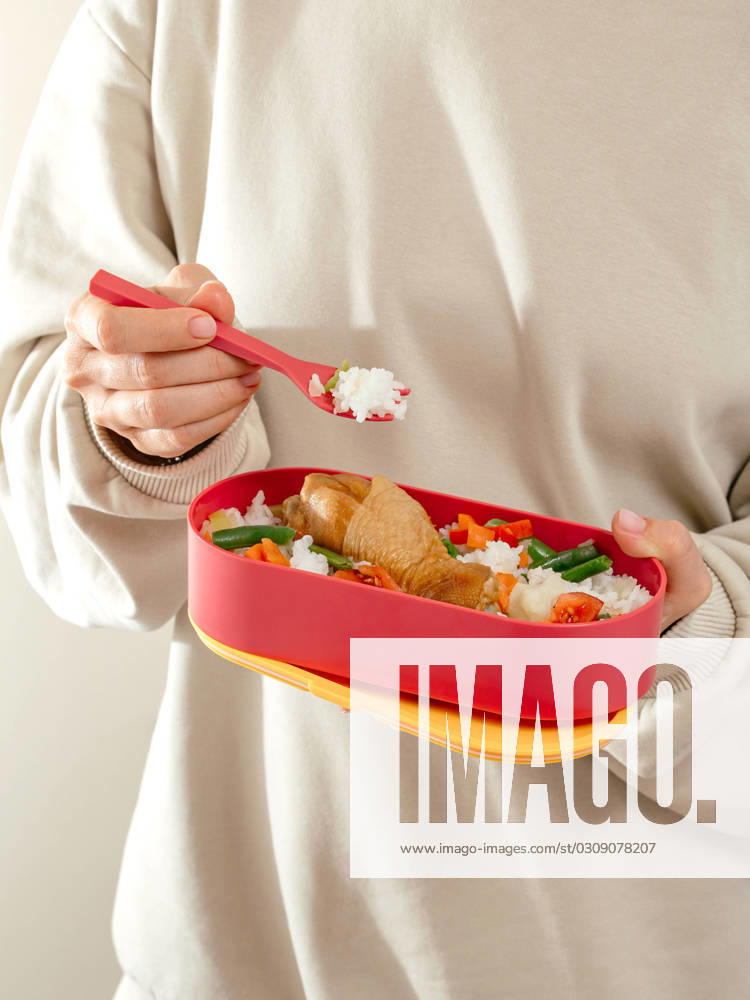 A girl eats food from a lunch box in the office. lunch box to th R_KUAL231016-1269580-01