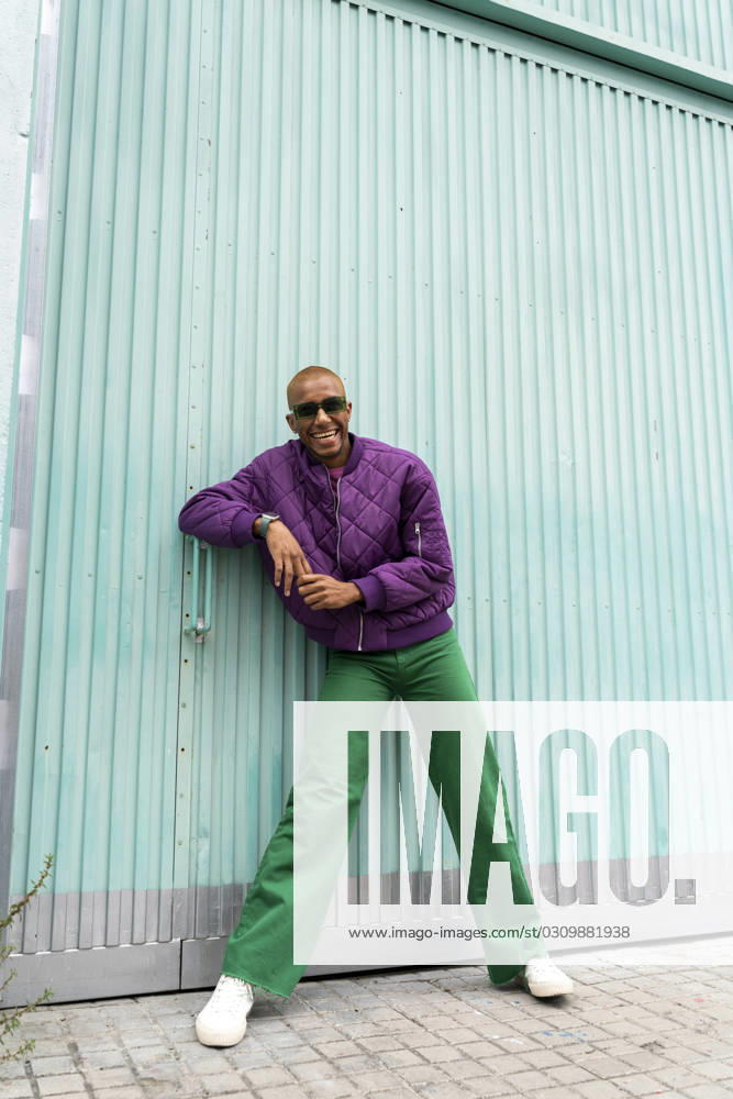 Happy non-binary person wearing sunglasses standing in front of blue shutter door model released, Symbolfoto, AFVF09370