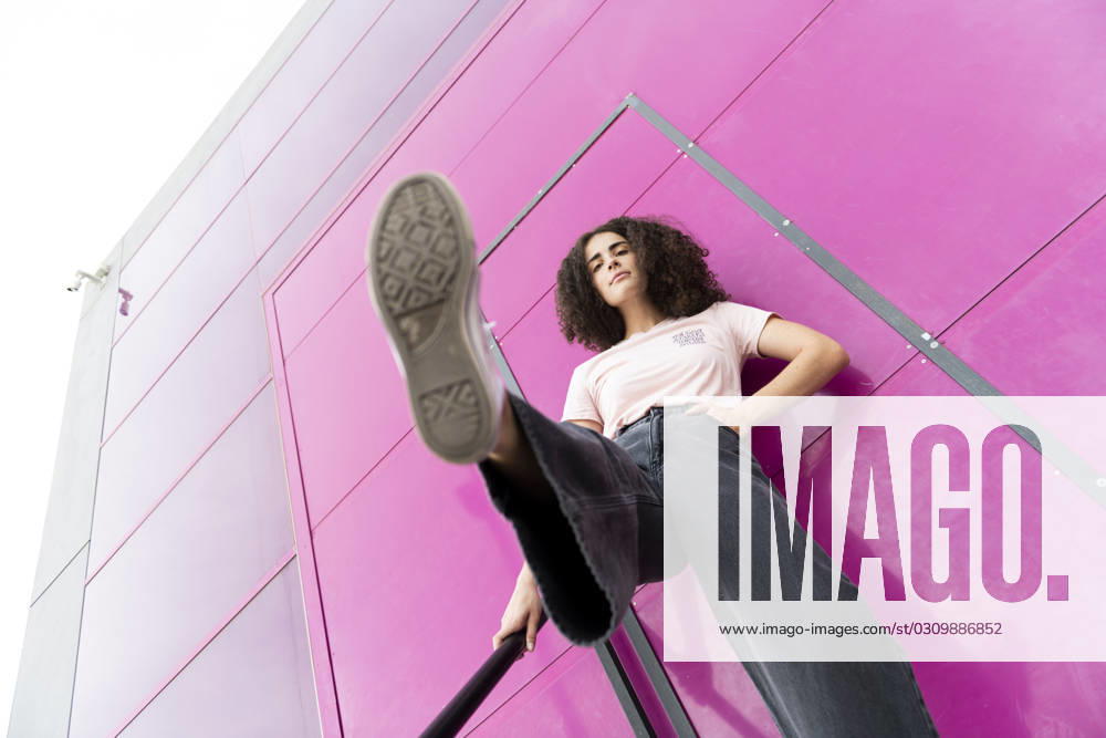 Young woman with leg up standing in front of pink door model released, Symbolfoto, LMCF00575
