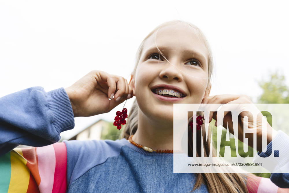 Smiling girl holding fresh redcurrants near ears model released, Symbolfoto, EYAF02846