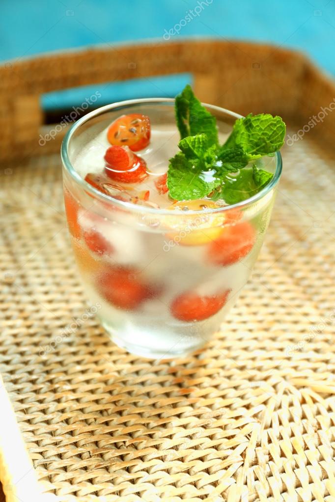Glass of cold refreshing summer drink with berries and ice cubes on table close up