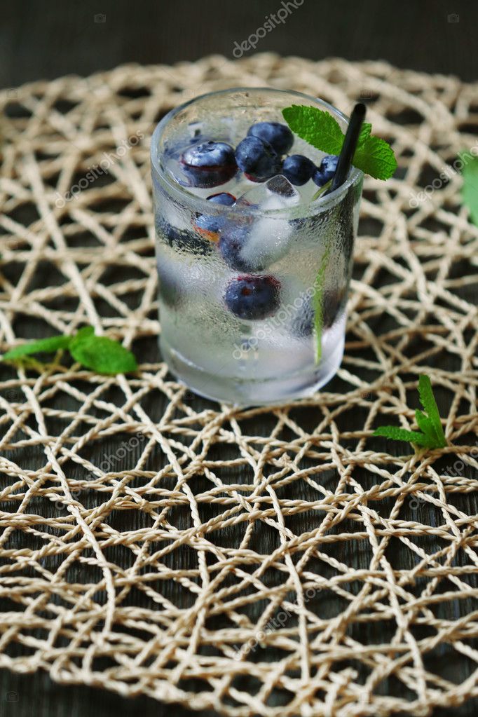 Glass of cold refreshing summer drink with berries and ice cubes on table close up