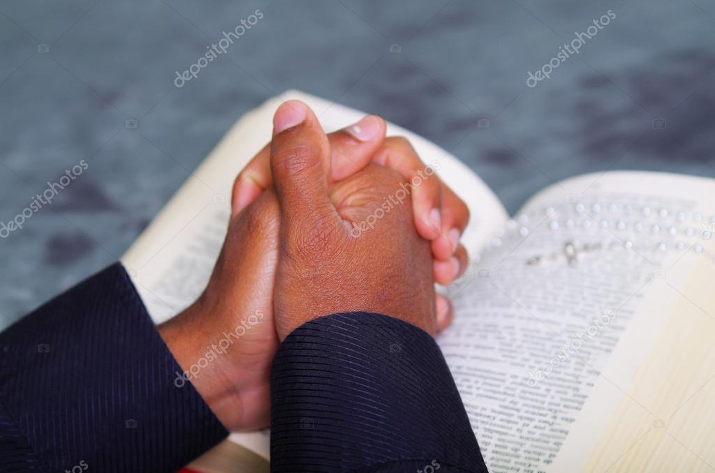Man folding hands praying with open bible lying in front, seen from behind models head, religion concept.