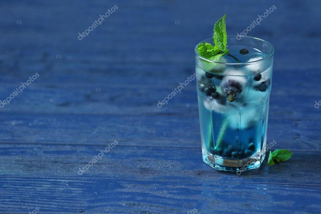 Glass of cold refreshing summer drink with berries and ice cubes on table close up