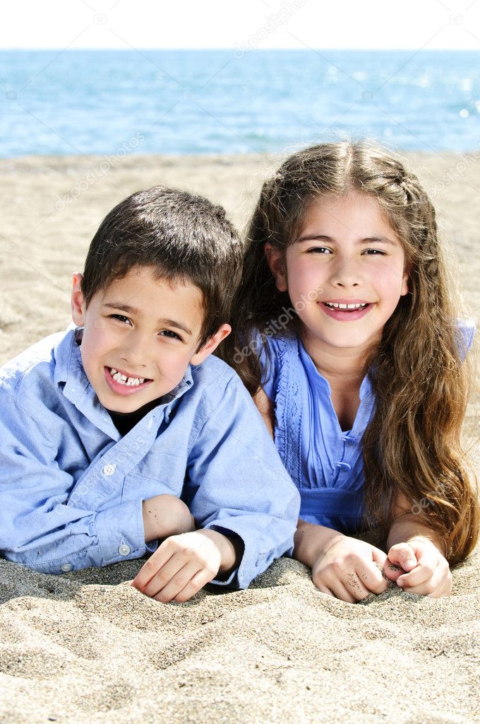 Portrait of brother and sister laying on sand at the beach model released