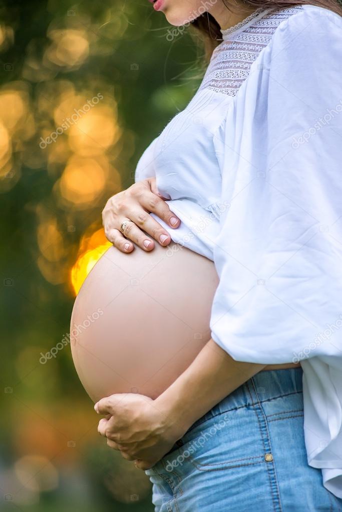 Pregnant woman walking in the park in the summer park. A girl prepares to become a mother. Walk in the fresh air.