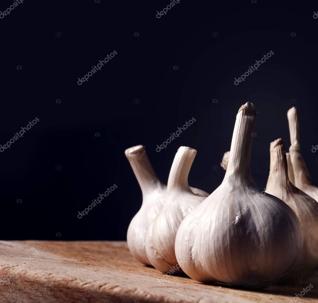 Garlic bulbs on rustic wooden cutting board. still life with dark copyspace. Aromatic food ingredients on kitchen table with black background. Garlic cloves spice prepared for cooking.