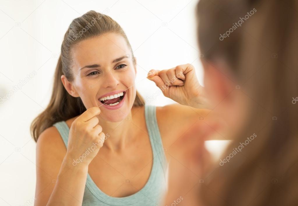 Portrait of young woman using dental floss in bathroom model released