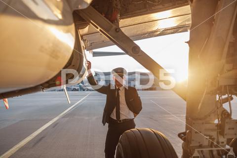 Professional male pilot in uniform and hat looking at camera, leaning on a big passenger airplane ready for departure in airport at sunset. Aircraft, occupation, transportation concept business, person, man, aerodrome, aeroplane, air, aircraft, airliner, airplane, airport, aviation, aviator, boarding, confident, corporate, crew, departure, elite, engineer, executive, expertise, flight, fly, flying, landing, jet, journey, lifestyle, lean on, looking, portrait, occupation, people, pilot, plane, standing, civil, professional, success, terminal, transport, transportation, travel, traveling, uniform, vehicle, horizontal