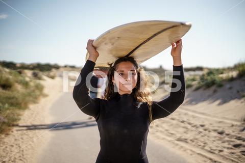 A shallow focus shot of a European female holding a surfboard and walking to the beach beach, nature, summer, sand, vacation, outdoor, holiday, day, people, sea, travel, beautiful, ocean, outdoors, young, woman, female, coast, lifestyle, white, recreation, outside, color, sun, background, casual, closeup, leisure, beauty, sky, green, sunny, sunlight, person, road, surfer, surf, board, european, shallow, focus, holding