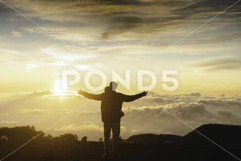 Full body back view of unrecognizable male traveler with spread arms while standing on top of mountain above cloudy sky at sundown time {{traveler,mountain,highland,nature,cloud,sunset,altitude,evening,peak,admire,freedom,mount,spain,tenerife,hiker,canary,sky,man,sundown,enjoy,high,spread arms,summit,dusk,adventure,top,activity,recreation,europe,spectacular,trip,travel,trekking,hike,journey,tourism,tourist,explorer,explore,height,horizontal,outside,unrecognizable,anonymous,faceless,full body,back view}}