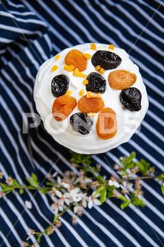 Easter cake, decorated with dried apricots and prunes, stands on a striped blue apron, a flowering branch. Easter religious holiday concept Easter, cake, holiday, tradition, traditional, decoration, multi colored, eggs, spring, celebration, watercolor, religion, food, icing, green, flower, prune, dried apricots, cream, sweet, festive, delicious, white, baked, pastry shops products, symbol, culture, table, sugar, dessert, bread, christianity, close up, decorative, bakery, glazed, biscuit, blue, colorful, season, pink, homemade, nobody, wooden, flora, plant, sand cover, brown, apron