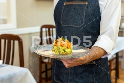 A waiter holding a plate with a salmon tartare with avocado and mango on it tartare, avocado, mango, fancy, appetizer, food, delicious, gourmet, tasty, waiter, meal, fresh, plate, snack, dish, hands, background, cuisine, eat, cream, restaurant, closeup, baked, healthy, lunch, dinner, nutrition, elegant, homemade, decoration, slice, sauce, fruits