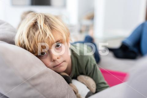 Unhappy boy with blond hair looking away while lying on comfortable gray sofa with toy in light living room on blurred background {{{boy,kid,unhappy,sad,couch,childhood,living room,unsatisfied,bored,rest,pastime,sofa,home,domestic,light,adorable,upset,apartment,blond,cute,displease,room,at home,appearance,flat,innocent,dissatisfied,calm,sweet,lounge,style,little,vulnerable,sensitive,comfort,apathy,charming,lifestyle,disappoint,attentive,mood,inside,looking away,blurred background}}}