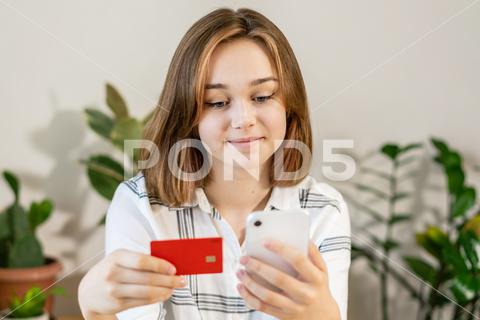Female professional doing online payment through credit card while sitting at home office. Cheerful young girl shopping or banking online using mobile phone and credit card, living room interior. modern, bank, sale technology, client contact, ecommerce mobile, digital insure, buyer person, millennials, gadget, exchange, transfer, tax, wireless, smartphone, ecommerce, paying, entrepreneur, freelancer, commerce, electronic, debit, digital, cvv, wallet, mobile, finance, laptop, woman, transaction, credit, pay, banking, store, sale, customer, card, e-commerce, lifestyle, money, buy, payment, credit card, retail, technology, shopping, internet, purchase, online, room with plants