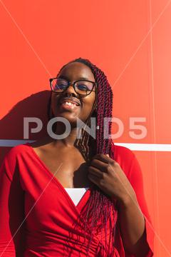 Cheerful young African American female in trendy outfit and glasses looking at camera while standing against red background portrait, black, woman, african american, style, trendy, red, female, outfit, modern, confident, fashion, urban, happy, cheerful, smile, model, elegant, street, bright, garment, apparel, vivid, positive, glad, optimist, feminine, content, color, vibrant, charming, lady, joy, cloth, copy space, colorful, personality, young, wall, enjoy, looking at camera, toothy smile, hairstyle, stand, outdoors, african, sunny, braids, monochrome