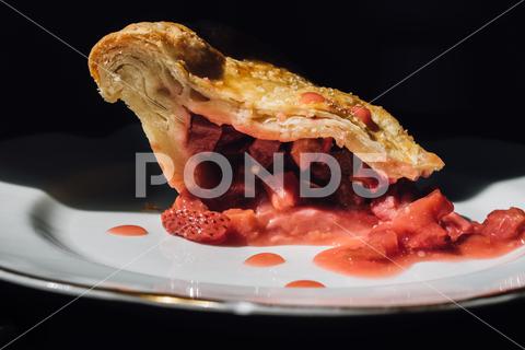 A side view of strawberry rhubarb pie slice on white plate with black background strawberry, rhubarb, pie, food, culinary, delicious, tasty, cuisine, fresh, dessert, pastry, bakery, sweet, baked, homemade, bake, snack, berry, fruit, ripe