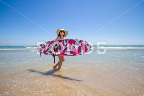A Hispanic woman wearing a swim wear while holding a surf board on the beach attractive, beach, coast, female, girl, happy, hispanic, holiday, leisure, lifestyle, ocean, people, person, pretty, sand, sea, summer, surf, swim, vacation, voard, water, wear, woman, young