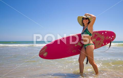 A Hispanic woman wearing a swim wear while holding a surf board on the beach attractive, beach, coast, female, girl, happy, hispanic, holiday, leisure, lifestyle, ocean, people, person, pretty, sand, sea, summer, surf, swim, vacation, voard, water, wear, woman, young
