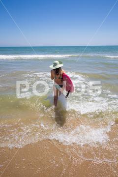 A Hispanic woman wearing swimwear while holding a surfboard on the beach attractive, beach, coast, female, girl, happy, hispanic, holiday, leisure, lifestyle, ocean, people, person, pretty, sand, sea, summer, surf, swim, vacation, voard, water, wear, woman, young