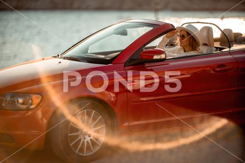 Outdoor summer portrait of stylish blonde woman driving red car convertible. Fashionable attractive woman with blond hair in a white hat in a red car. Sunny bright colors taken outdoors against the sea red, car, convertible, vehicle, stylish, hat, blonde, fair, portrait, hair, attractive, outdoors, woman, adult, pose, posing, pretty, sunglasses, model, drive, fashion, automobile, person, style, long, people, auto, street, nice, trip, sea, elegance, traveler, beautiful, glamour, background, rocks, cute, driver, women, lady, tourism