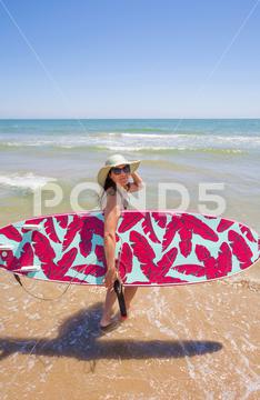 A Hispanic woman wearing swimwear while holding a surfboard on the beach attractive, beach, coast, female, girl, happy, hispanic, holiday, leisure, lifestyle, ocean, people, person, pretty, sand, sea, summer, surf, swim, vacation, voard, water, wear, woman, young