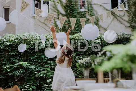 Rear view of happy little child playing with a wedding decorations. {wedding,celebration,guest,girl,playing,decorations,playful,enjoy,dancing,table,wedding reception,party,garden,dining table,food and drink,kid,backyard,life events,happiness,enjoyment,ceremony,decoration,reception,birthday,outdoors,happy,cheerful,joy,dance,baloons,rear view,carefree,small,banquet,flower,decor,event,white,glass,outdoor,romantic,setting,arrangement,green,romance,bouquet,celebrate}